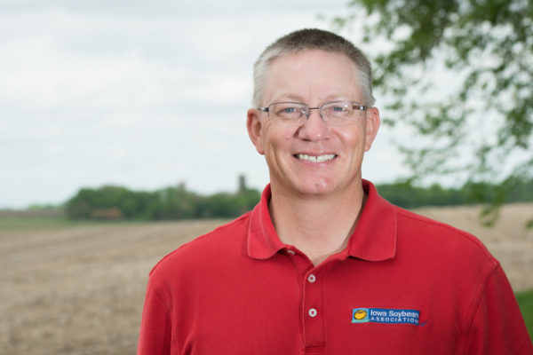 Tom Oswald smiles, standing in front of an open corn field.