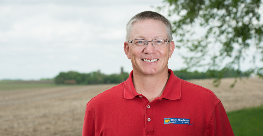 Tom Oswald smiles, standing in front of an open corn field.