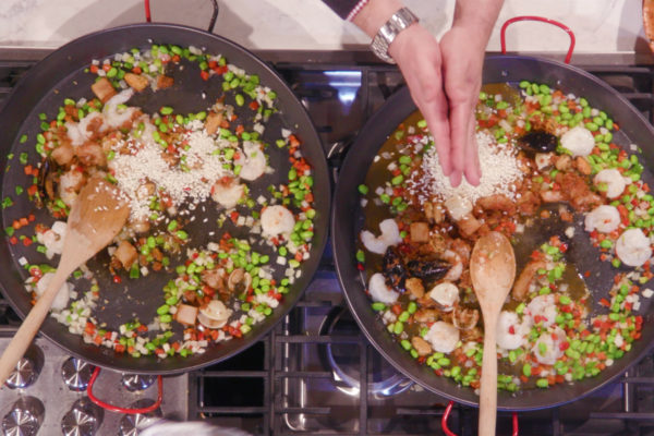 A chef cooks two pans full of seafood and edamame.