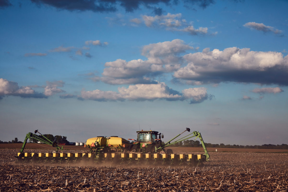 A green and yellow soy planter drives through a field full of corn stubs.