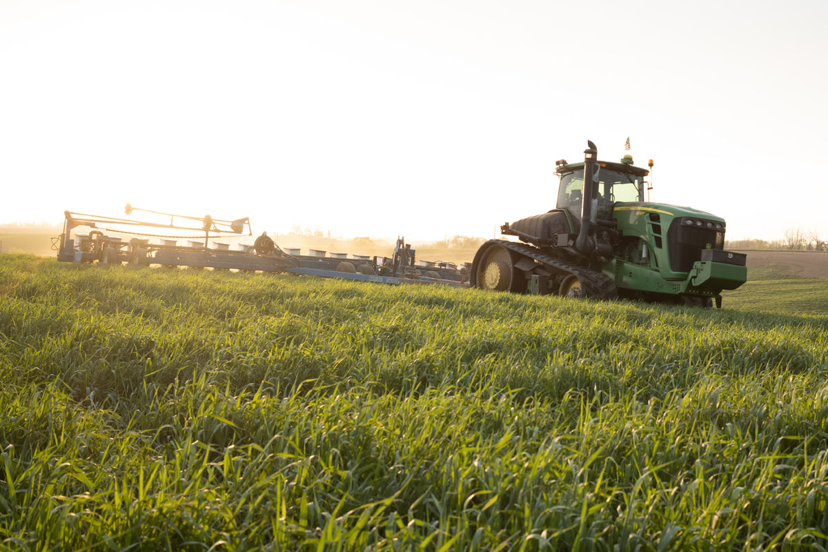 A John Deere tractor pulls a seed planter in a grass field.