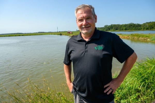 Phillip Good, a USB farmer-leader, stands in front of a large aquaculture farm.