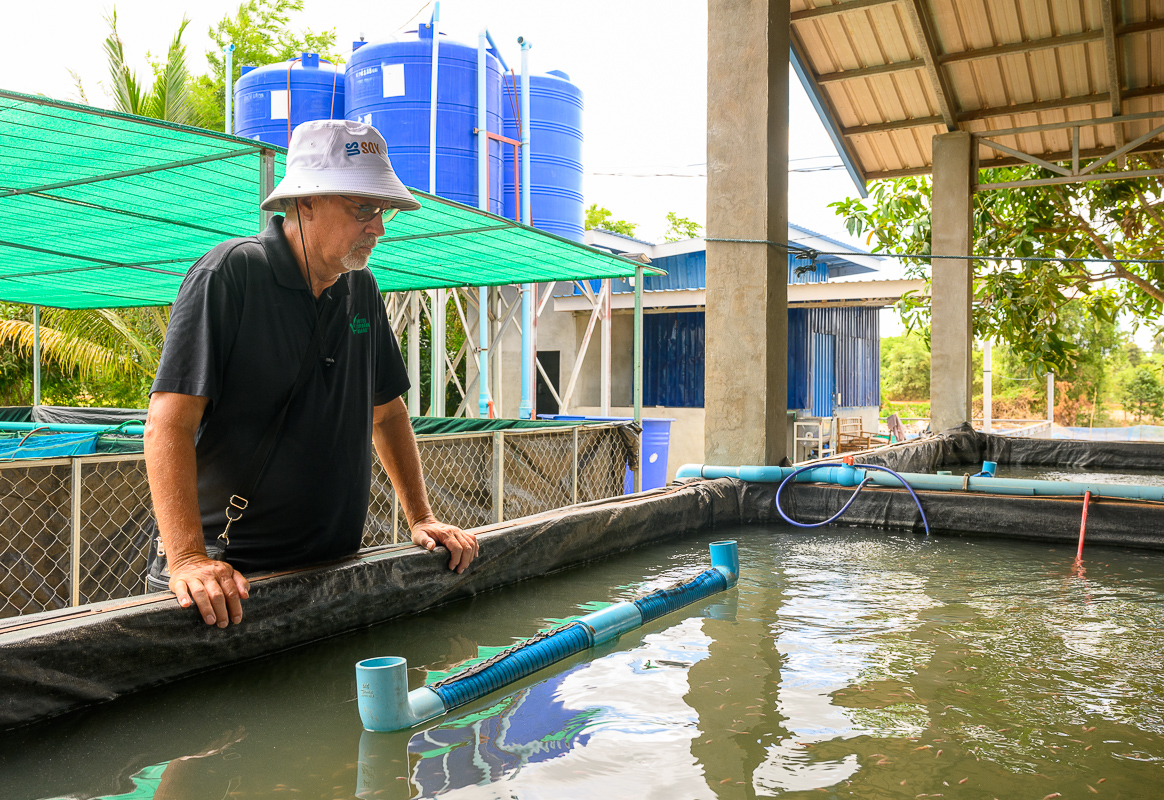 A USB representative attentively observes an aquaculture tank filled with small orange fish.