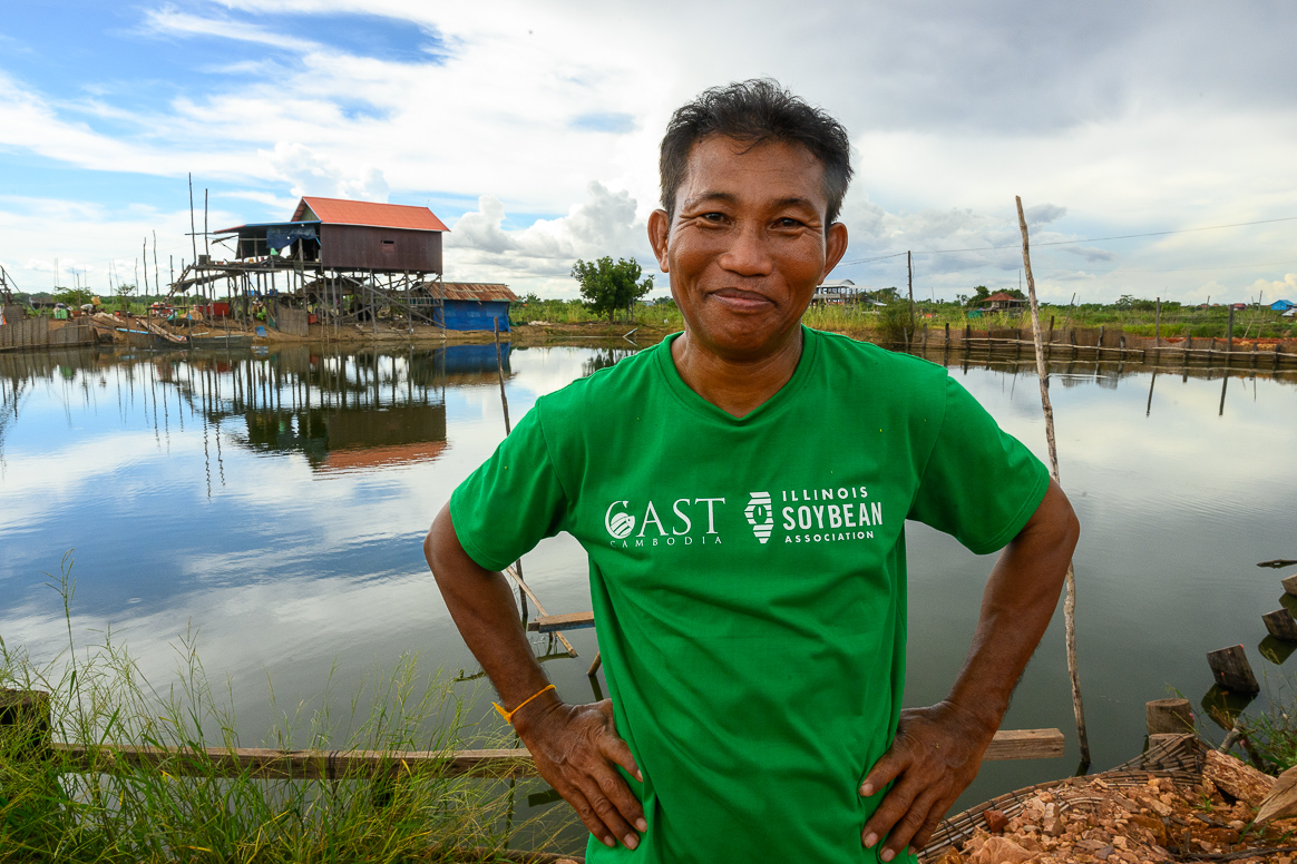A Cambodian citizen stands in front of a lake, wearing an Illinois Soybean Board T-Shirt.