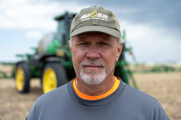 A close-up of a farmer in front of his John Deere tractor in a field.