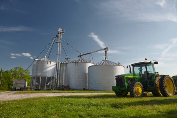 A green tractor sits in front of soybean grain bins.