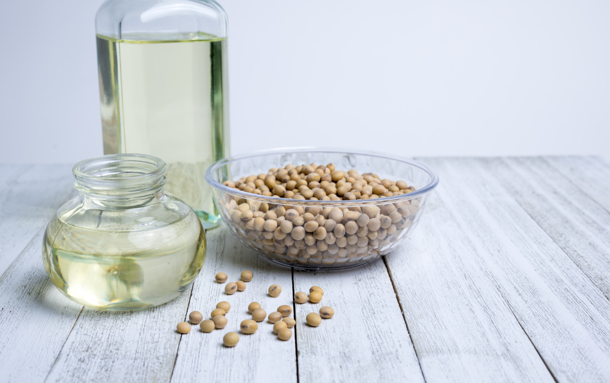A bowl of soybeans and two soybean oil jars sit on a gray wooden counter.