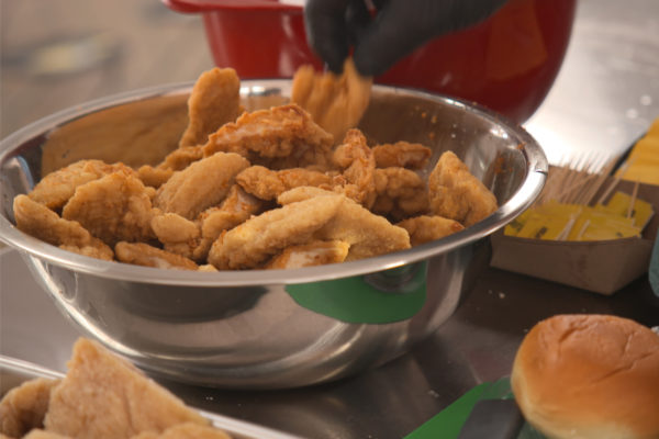 A chef places breaded fried chicken into a stainless-steel bowl.
