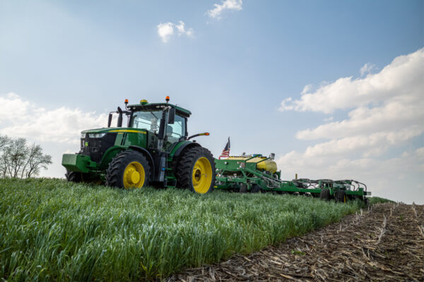 A farmer driving a tractor and using a planter to plant soybean seeds into a field of cover crops, illustrating sustainable farmer practices.